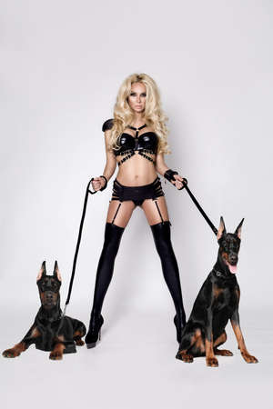 Sexy blonde model in erotic lingerie and latex stockings with doberman dogs isolated on white background. Hot lingerie model. Sensual woman with dogs.の写真素材