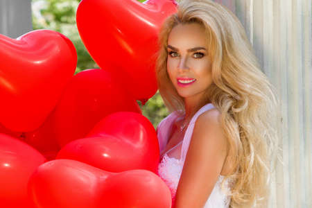 Bride in a wedding dress is walking in a beautiful garden and holding red balloons. Set of Air Balloons. Wedding fashion. Valentines day and bride at the wedding party.の写真素材