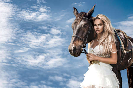 Portrait of a dark horse and woman. Beautiful glamor woman with a horse. Portrait of a beauty blonde bride in wedding dress with horse.の写真素材