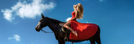 Portrait of a dark horse and woman. Beautiful glamor woman with a horse. Portrait of a beauty blonde in red sexy dress with horse. Amazon on horse.の写真素材