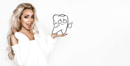 Beautiful young happy woman with a beautiful white smile is holding tooth on white background. White teeth. Dentist concept.の写真素材