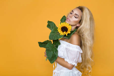 Beautiful woman posing with yellow sunflower on yellow pastel studio background. Concept of women's and mother's day. Spring, summer feelings. Girl power. Spring fashion.の写真素材