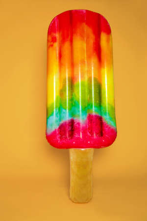 Colorful inflatable beach mattress, isolated on yellow background. Air mattress. Inflatable mattress in form of colorful ice cream. Summertime.の写真素材