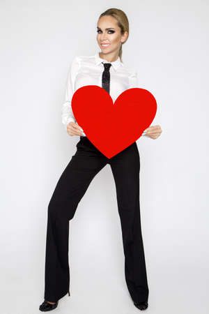 Valentine's Day. Elegant woman with red heart isolated on white background. Sexy woman in elegant suit and tie is holding big heart. Holiday party, birthday. Valentine's day- concept.の写真素材