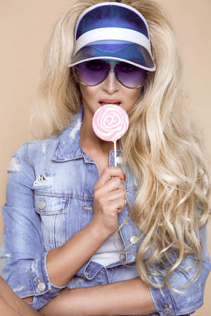 Sexy blonde model dressed in a jeans jacket and shorts on beige, pastel background. Jeans fashion model. Spring summer fashion.の写真素材