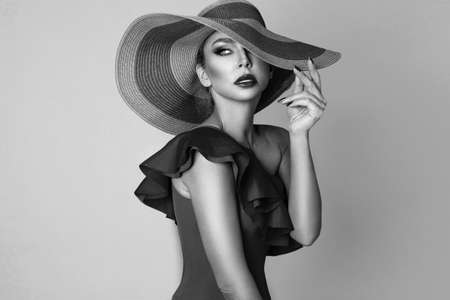 Elegant woman in a hat and bikini on a white background in studio. Black and white photo. Bikini fashion. Swimsuit fashion. Elegance.の写真素材