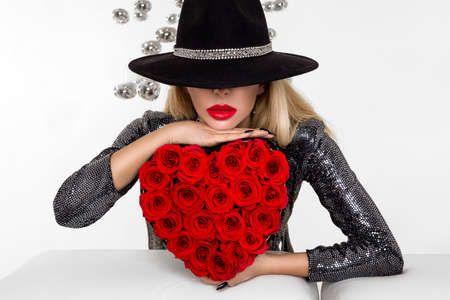 Valentine Beauty girl with red heart roses. Portrait of a young female model with gift and hat, isolated on background. Beautiful Happy Young woman presenting flower box. Holiday party, birthday.の写真素材