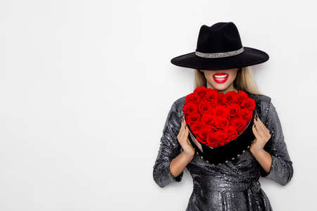 Valentine Beauty girl with red heart roses. Portrait of a young female model with gift and hat, isolated on background. Beautiful Happy Young woman presenting flower box. Holiday party, birthday.の写真素材