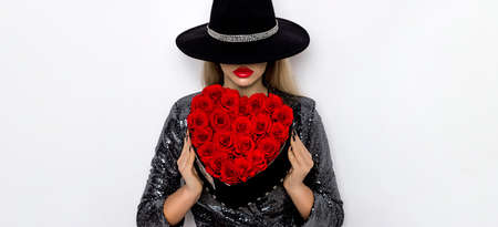 Valentine Beauty girl with red heart roses. Portrait of a young female model with gift and hat, isolated on background. Beautiful Happy Young woman presenting flower box. Holiday party, birthday.の写真素材