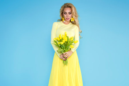 Spring fashion Woman. Beautiful happy woman with colorful dress, holding a bouquet of spring flowers on blue background in studio. Fashion photo. Spring flowers - concept. Woman with Easter tulips.の写真素材
