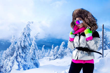 Young woman winter portrait. Winter fashion model with ski suit and goggles. Attractive young woman in wintertime outdoor. Mountains, white snow in magic winter day. Mountain climbing - concept.の写真素材