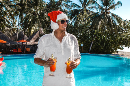 Christmas Santa Claus on the pool at the ocean. Christmas Maldives beach. Santa Clause hat male model in the Maldives holds drinks. Happy New Year travel space for hot countries concept - imageの写真素材