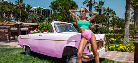 Bikini fashion. Beautiful sexy blonde woman in colorful swimsuit near the pink car on Cuba Havana. Spring and summer fashion model concept. Vintage and retro style.の写真素材