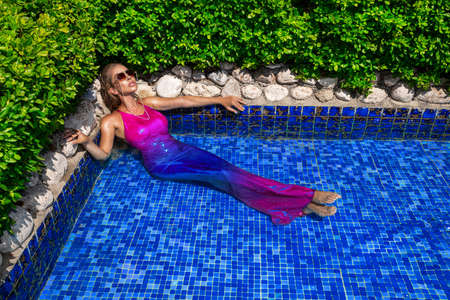 Summer fashion. Sexy fashion model. Glamor, stylish sexy blonde female model in elegant colorful dress in the pool. Travel model in a luxury hotel in Miami Florida. Siren.の写真素材
