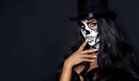 Beautiful model in Halloween makeup on black background. Sexy woman in top hat and skull makeup....