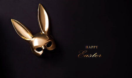 Easter background with gold bunny mask decor. Top view with copy space. Minimalism. Happy Easter. Gold mask on black background.の写真素材