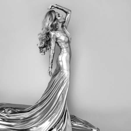 Elegant fashion. Stunning blonde woman in elegant long dress and perfect hairstyle on white background. Luxury evening fashion. Glamor fashion model. Elegance. Golden dress. Black and white art photo.の写真素材