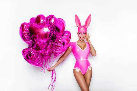 Sexy blonde woman posing in latex pink costume and pink bunny mask and pink balloons on white background. Easter bunny concept. Latex lingerie. Naughty girl. Halloween costume. Woman with balloons.の写真素材