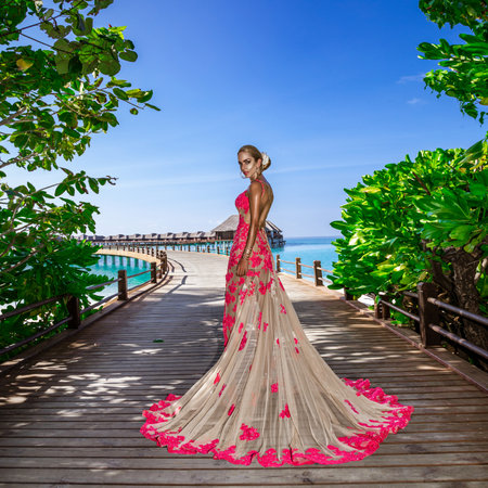 Luxury fashion. Elegant fashion model is posing outdoor. Stylish female model in long gown dress on the Maldives beach. Elegance. Classy woman in amazing dress on Maldives landscape. Couture. Vogue.の写真素材