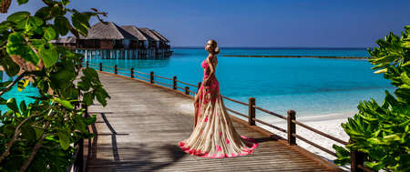 Luxury fashion. Elegant fashion model is posing outdoor. Stylish female model in long gown dress on the Maldives beach. Elegance. Classy woman in amazing dress on Maldives landscape. Couture. Vogue.の写真素材