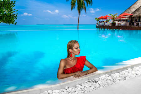 Elegant tanned woman in red swimsuit in pool on tropical Maldives island. Beautiful bikini girl in pool with view on horizon. Sexy model near the pool on beautiful Indian ocean landscape. Travel.の写真素材