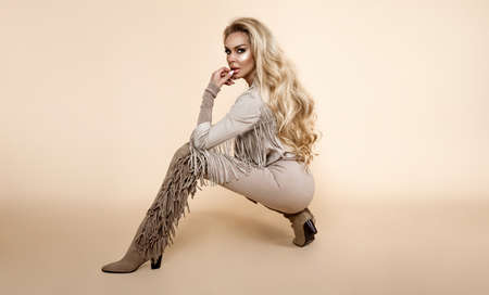 Spring fashion. Beautiful stylish female model in beige trendy clothes in studio. Elegant woman in stylish outfit and fringe boots on beige background. Studio shoot. Fashionable woman. Country styleの写真素材