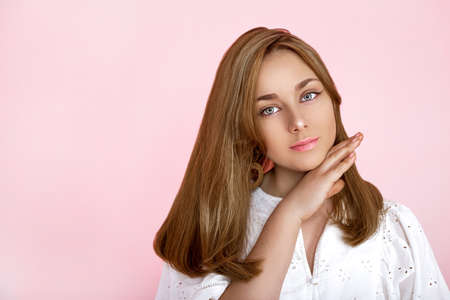 Portrait of a beautiful natural and smiling girl on a pink background. Beautiful young girl with perfect face and beautiful hair is posing in studio. Beauty, makeup, hair. Perfect face.の写真素材