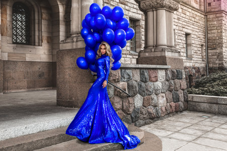 Elegant luxury fashion. Glamor, stylish elegant woman in long gown sequin dress is holding bunch of balloons. Female model in sequin long dress in the park. Outdoor shoot. Girl with balloons. Vogue. Couture.の写真素材