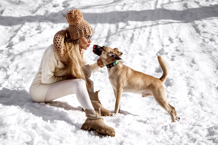 Beautiful stylish woman playing with her dog in the snow in winter scenery in the mountains. Winter vacation.の写真素材