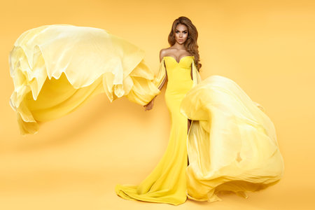 Fashion Woman in Yellow Fluttering Dress. Glamor Model is posing in Long Silk Fabric flying on Wind. Elegance.の写真素材