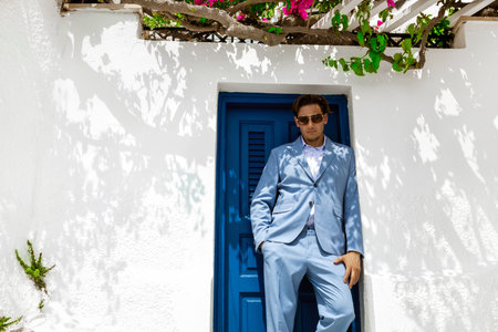 Elegant handsome man in blue suit is posing near in Fira in Santorini. Groom. Engagement and wedding in Santorini island of Greece.の写真素材