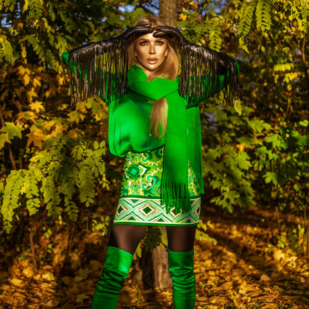 Beautiful female model wearing elegant autumn winter outfit, fashionable accessories and green scarf is posing in park on a sunny day.の写真素材