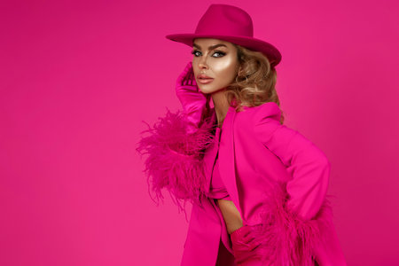 Glamor female model is wearing an elegant fuchsia suit, pink booties and a pink handbag with spring flowers and is posing against a pink background.の写真素材