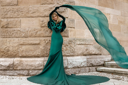 Elegant luxury evening fashion. Glamour, stylish elegant woman in green long evening gown dress is posing in the city outdoor. Female model in amazing long dress. Outdoor shooting. Vogue. Couture.の写真素材