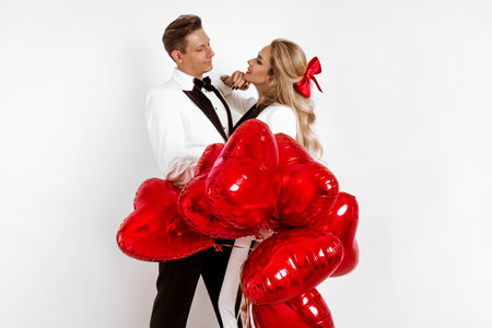 Happy beautiful couple in love posing on white background and holding red Valentine's Day heart balloons. Romantic photo for Valentine's Dayの写真素材