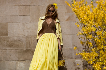 Summer fashion model in flowing yellow maxi dress poses in the city on a sunny summer day.の写真素材