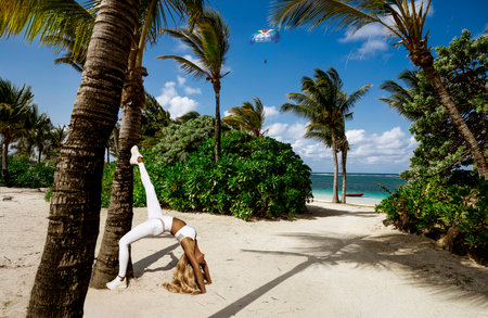 Athletic woman practicing yoga on a tropical beach in Mauritius, wearing white fitness outfit....