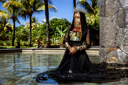 Majestic Woman in Black and Gold Royal Costume With Crown and Mask in Tropical Mauritius Resort...