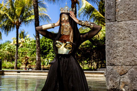 Majestic Woman in Black and Gold Royal Costume With Crown and Mask in Tropical Mauritius Resort...