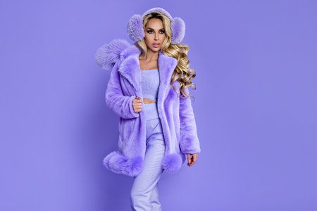 Happy Fashion Woman in Pastel Lilac Faux Fur Coat and Fluffy Earmuffs on Matching Purple Background, Cozy Winter Monochrome Beauty Portraitの写真素材