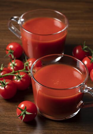 Tomato juice and fresh tomatoes placed against a tree background, photographed from an angle.の写真素材