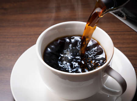 Pouring hot coffee against a dark wooden backdropの写真素材