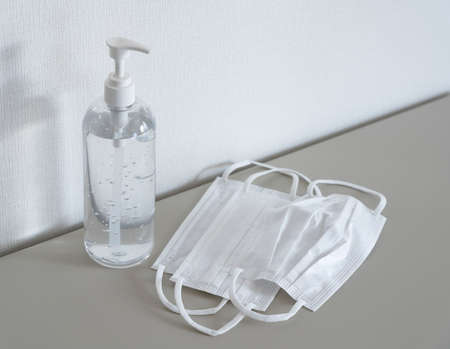 Sanitizing gel and mask placed in front of a white wall. Image of an antivirus