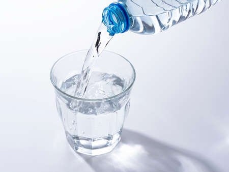 Pour bottled water into a clear glass placed on a white background.