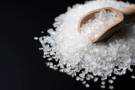 Himalayan rock salt and a scoop of wood placed on a black background