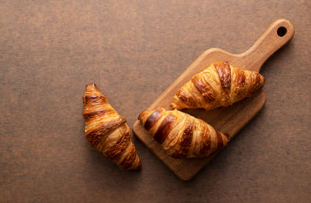 Croissant placed on a wooden chopping board with a wooden background. View from above