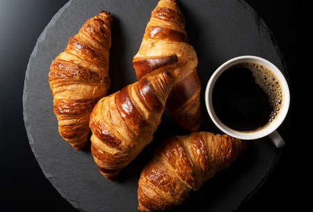 Croissants and hot coffee on a black stone plate with a black background. A view from above