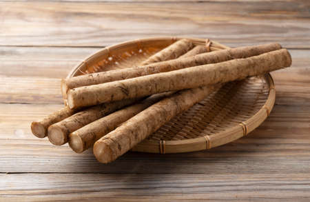 Burdock in a bamboo colander placed in the background of a wooden boardの写真素材