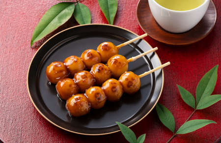 Mitarashi dango and green tea on a red Japanese tray. Image of mitarashi dango, a Japanese sweet