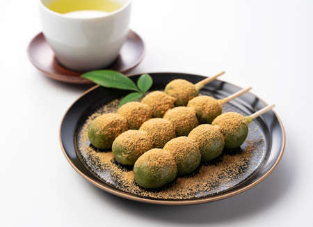 mugwort-flavored rice dumpling covered with soybean flour and green tea served on a black plate set...